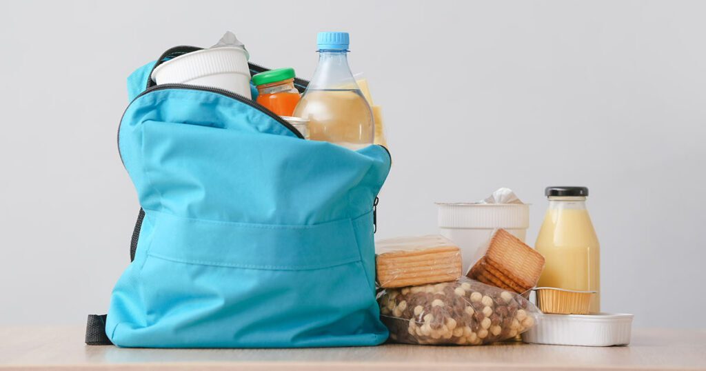 Blue backpack with food stuffed inside and next to the backpack. This is part of a school backpack food program.