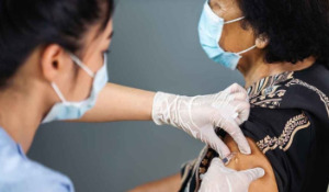 Thumbnail photo of woman in mask and surgical gloves giving another woman in a mask a Covid-19 vaccine.