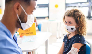 Thumbnail photo of male doctor in mask talking to a tween child who is also wearing a mask.