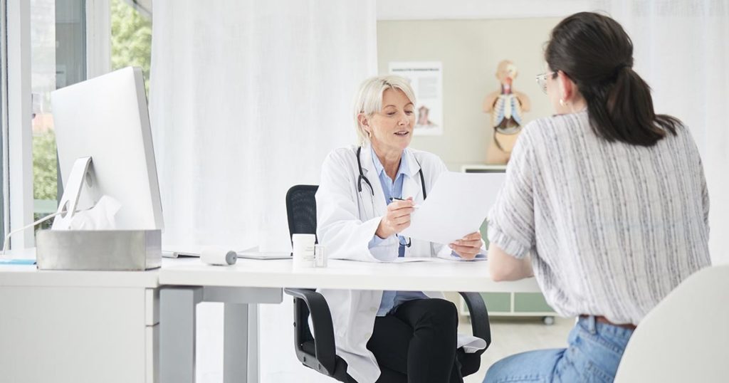 Doctor sitting at desk with patient, and she is giving the woman a consultation.