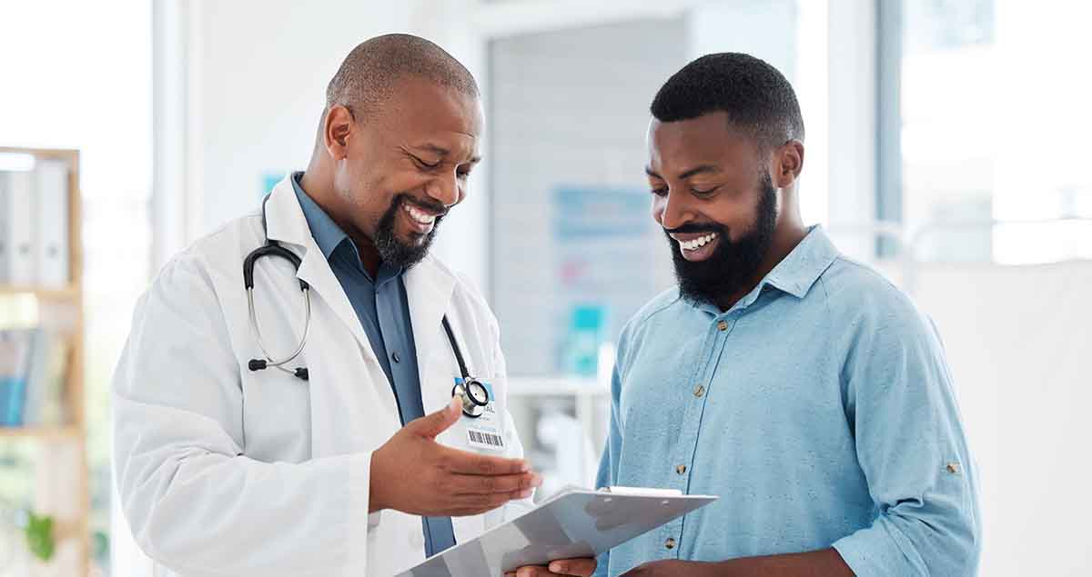 Young patient in a consult with his doctor. African american doctor showing a patient their results on a clipboard. Medical professional talking to his patient in a checkup.