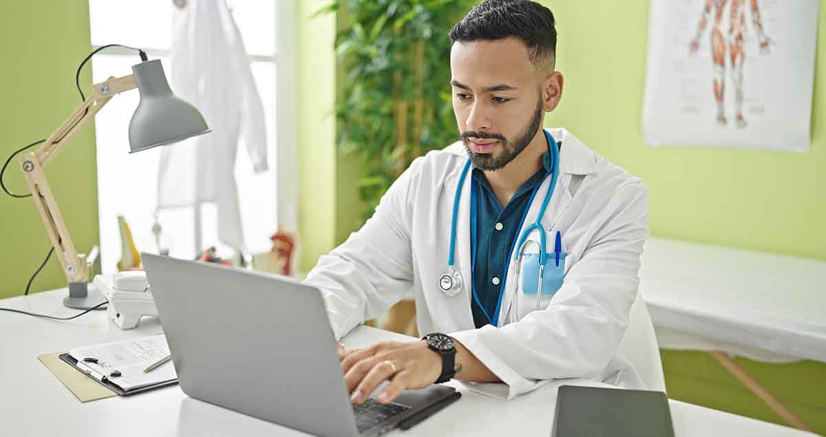 Young hispanic man doctor using laptop working at clinic