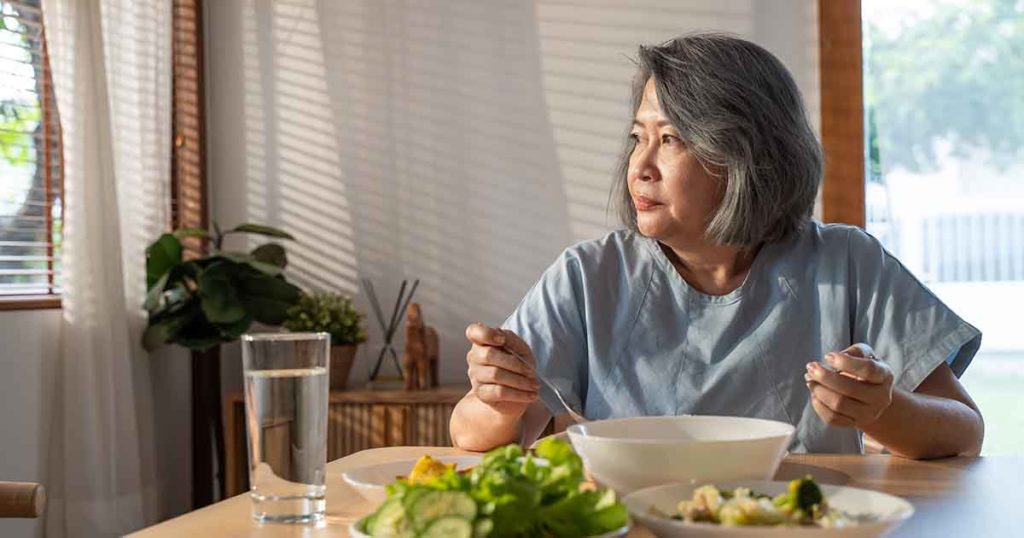 Elderly asian woman eating at dinner table thinking