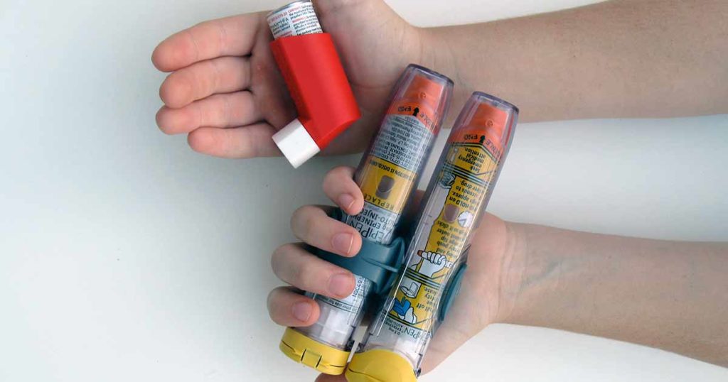 Kids hands holding two epipens in one and an inhaler in the other