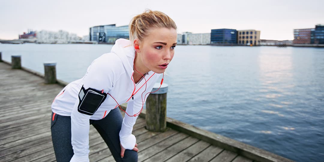 photo of Female runner standing bent over and catching her breath after a running session along river.