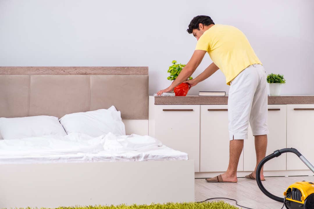 Young handsome man cleaning in the bedroom