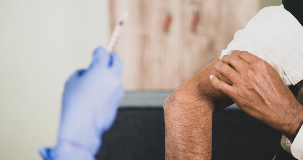 Man with rolled up sleeve is ready to receive his weekly allergy shot in order to build an immunity to seasonal allergies. There is a hand with a medical glove holding up a syringe.