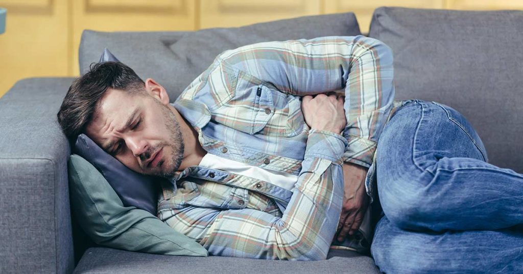 Man laying on his couch holding his abdomen in discomfort.