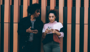 Thumbnail photo of Black couple looking at their phone while leaning against a fence.