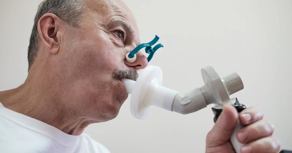 Older hispanic man using a spirometer to test for asthma at a doctor