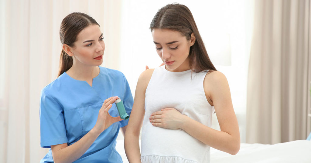 Young pregnant woman on hospital bed with doctor showing her how to use her asthma medication.