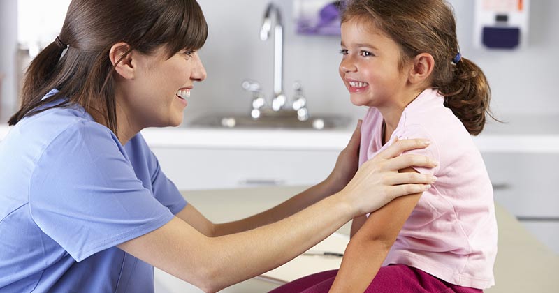 School nurse holding the arms of a young student and is facing the student. They are both smiling and relieved.