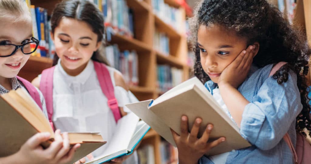 Photo of three young girls in the school library reading books.