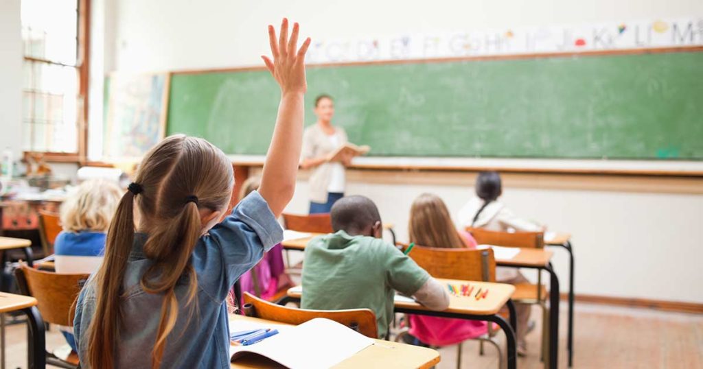 Classroom of tweens with a girl raising her hand in the back