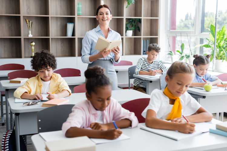 Photo of teacher standing in a classroom with students at their desks.