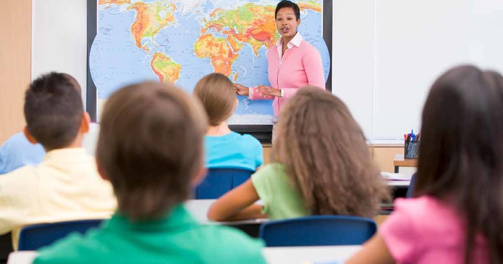Teacher at the front of the class showing students a world map