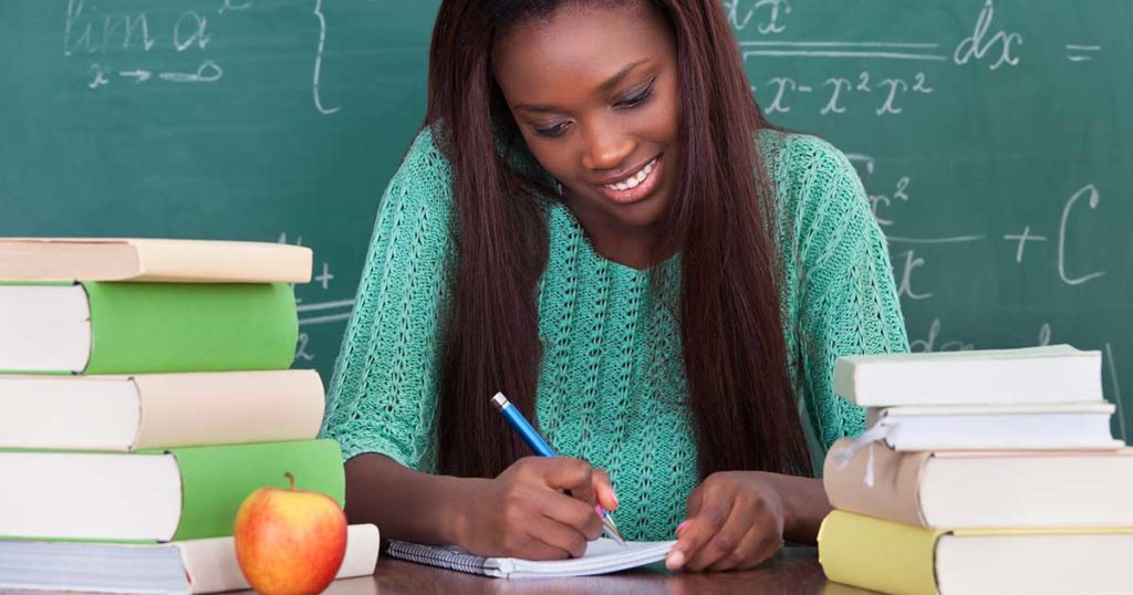 Teacher smiling at desk while writing reports out