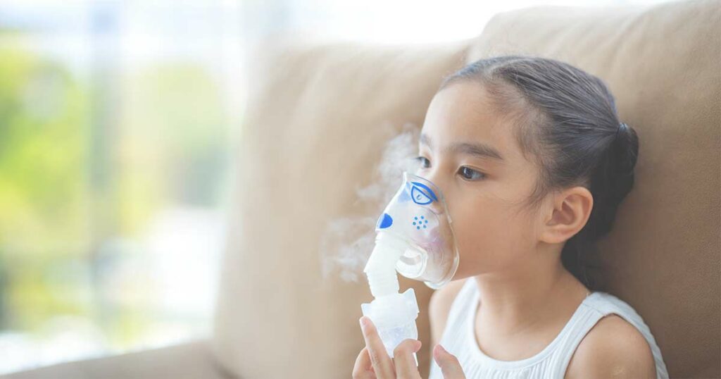 Tween girl sitting on a big soft chair with an asthma inhaler mask on. She is getting a nebulizer treatment.