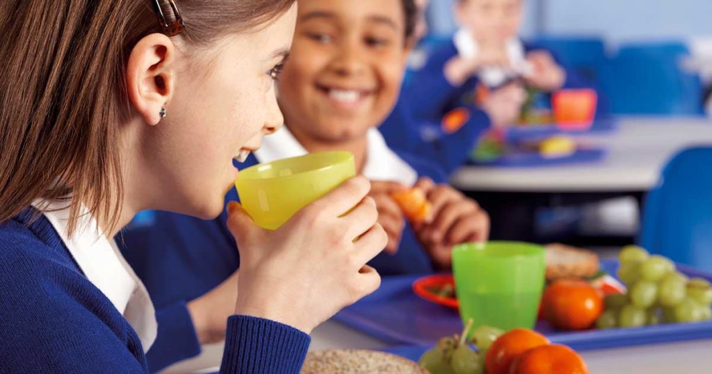 A boy and girl sitting in the school lunchroom, eating, and smiling.