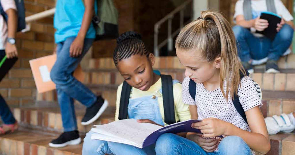 Two girls sitting on school steps looking at a notebook together