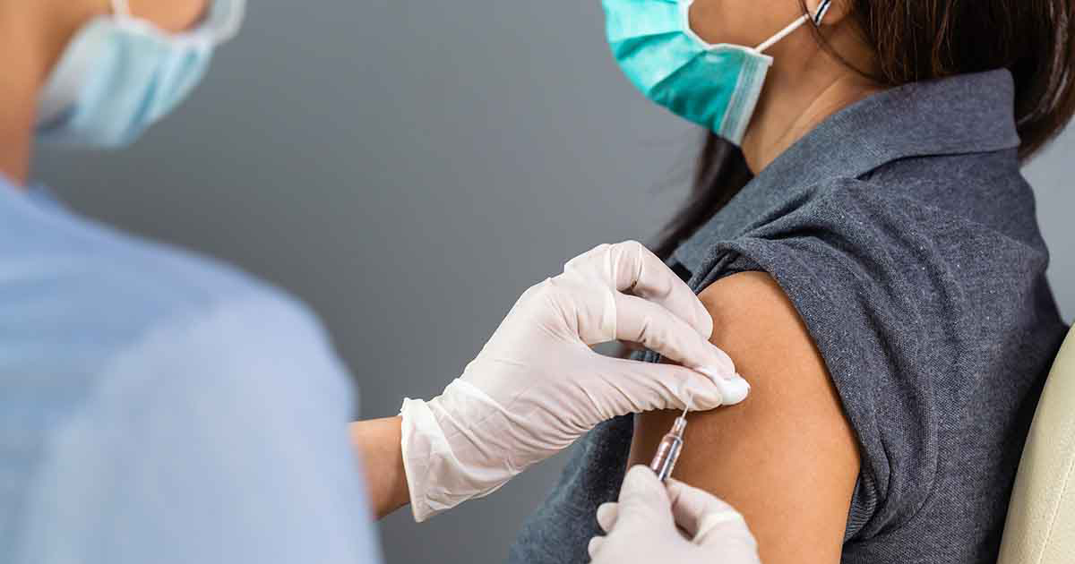 Photo of woman with her sleeve rolled up getting a COVID-19 vaccination by a woman doctor. They are both wearing masks.