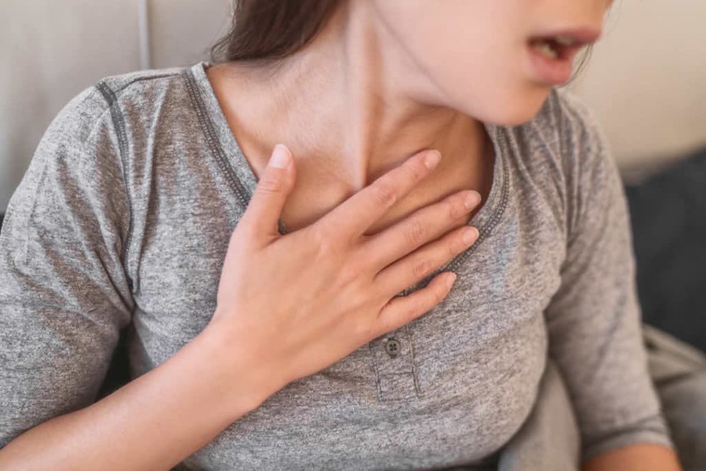 Woman holding her chest with her mouth open. Her neck looks stressed because she