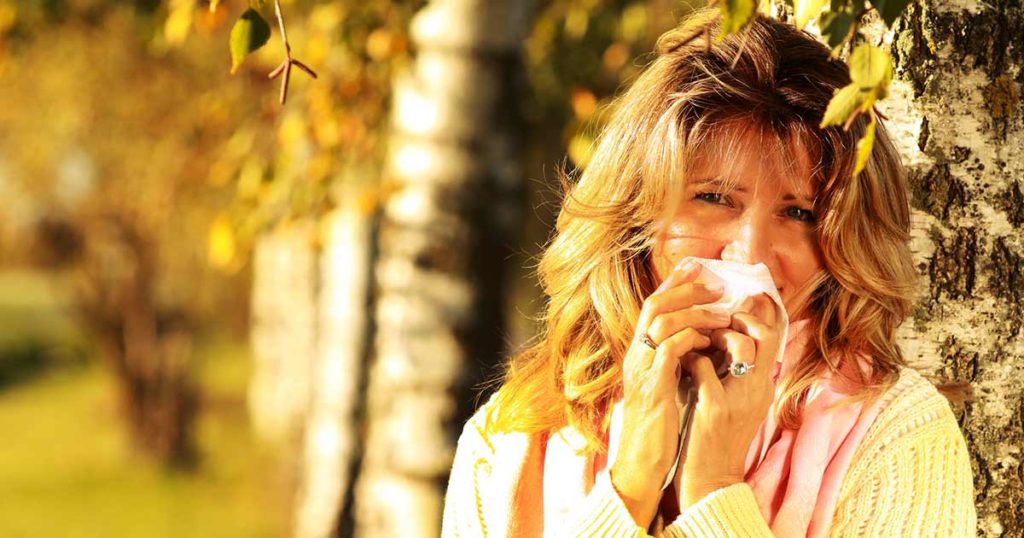 Woman with Birch tree allergy, holding a tissue to her nose.
