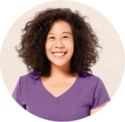 Image of mixed race Black and Asian woman wearing a purple shirt and a big smile