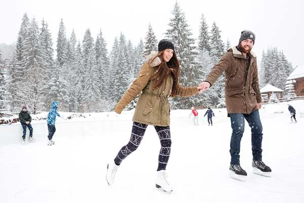 People at an outdoor skating rink. The foreground has a young couple holding hands.