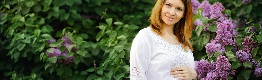 Pregnant woman outside in front of a lilac bush