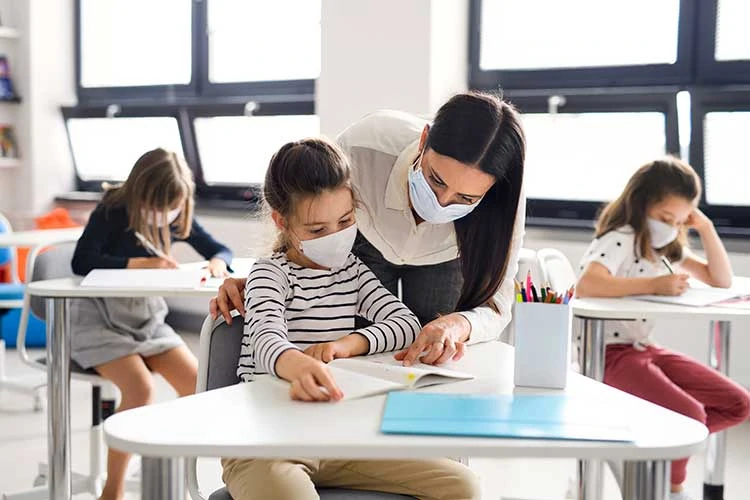 Photo of classroom with children at their desks wearing masks. Teacher also has a mask.