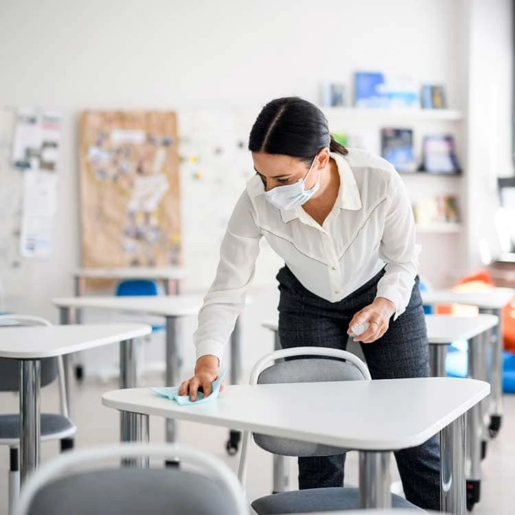 Teacher wiping down classroom desks. She