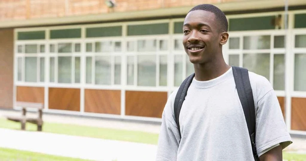 Photo of teenage black boy standing outside in front of a school