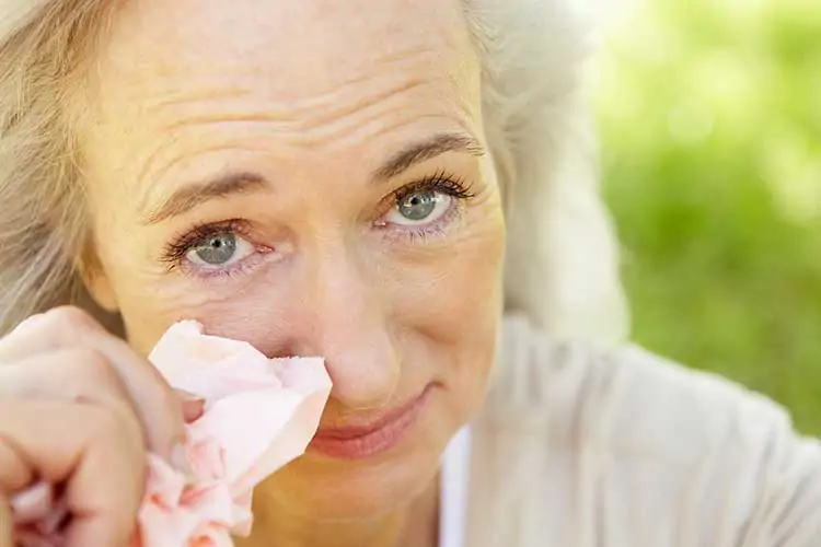 Image of older woman with itchy eyes, holding a tissue, because of allergies.