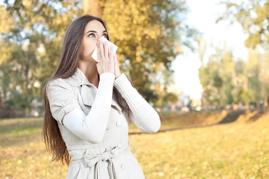 Photo of woman with tissue to her nose while she is having an allergic reaction to hay.