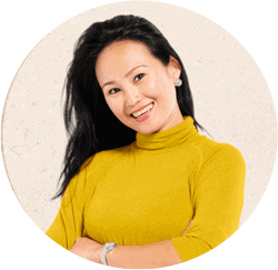 Portrait of young Asian woman smiling. She has long dark hair and is wearing a yellow sweater